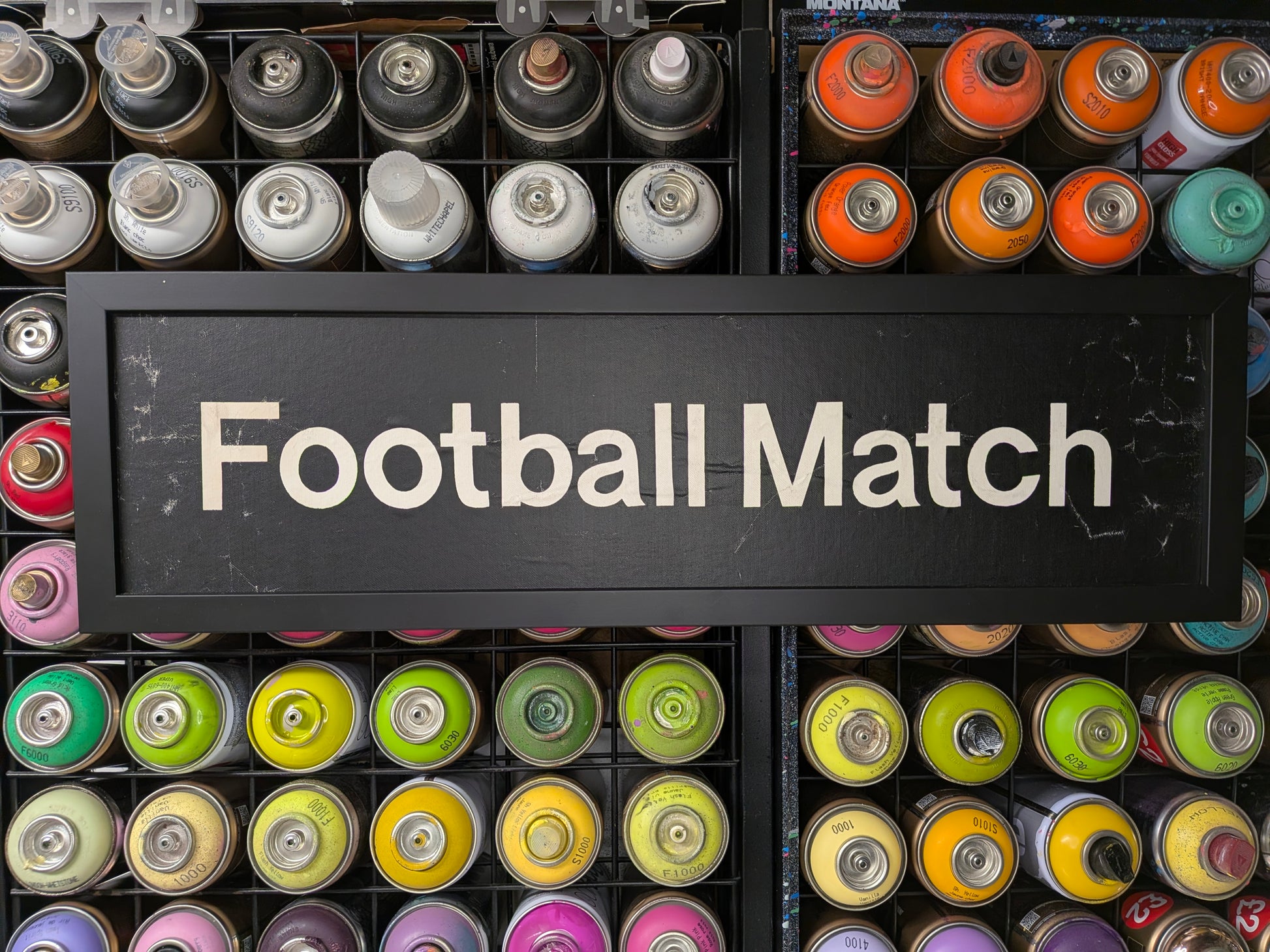 Colorful spray paint cans with a sign reading 'Football Match' on a black background.