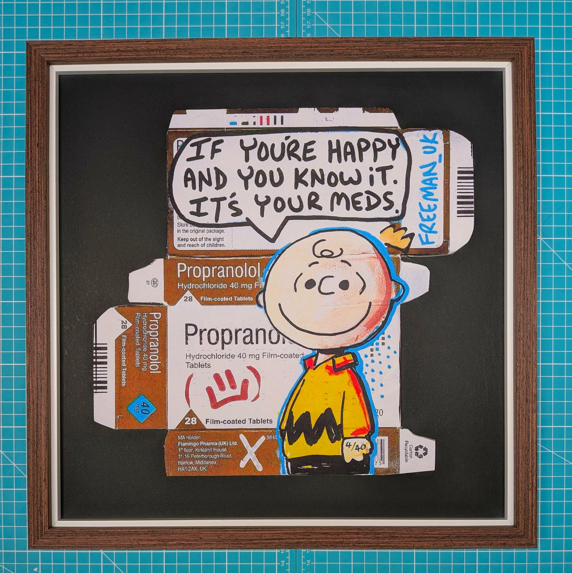 A framed art print featuring a cartoon illustration of Charlie Brown from Peanuts layered over printed Propranolol and Freeman US medicine boxes, with a speech bubble reading 'IF YOU'RE HAPPY AND YOU KNOW IT. IT'S YOUR MEDS.