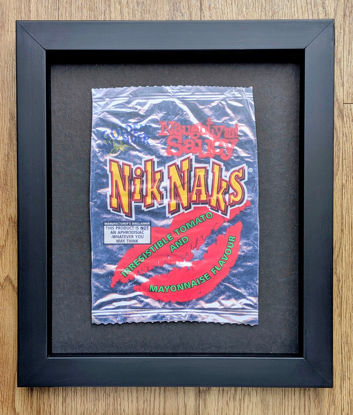 Framed vintage-style product packaging of Nik Naks on a wooden surface