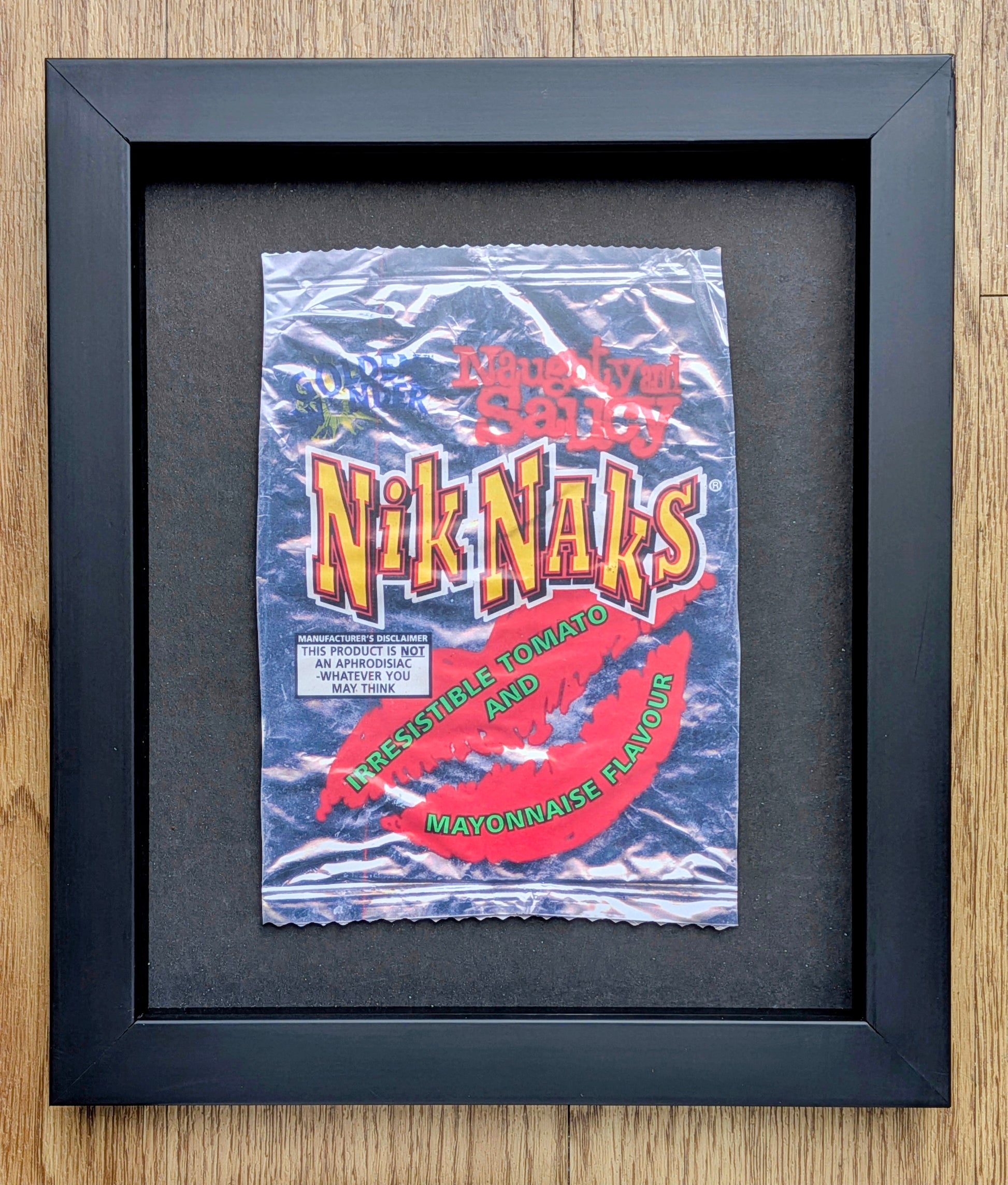 Framed vintage-style product packaging of Nik Naks on a wooden surface