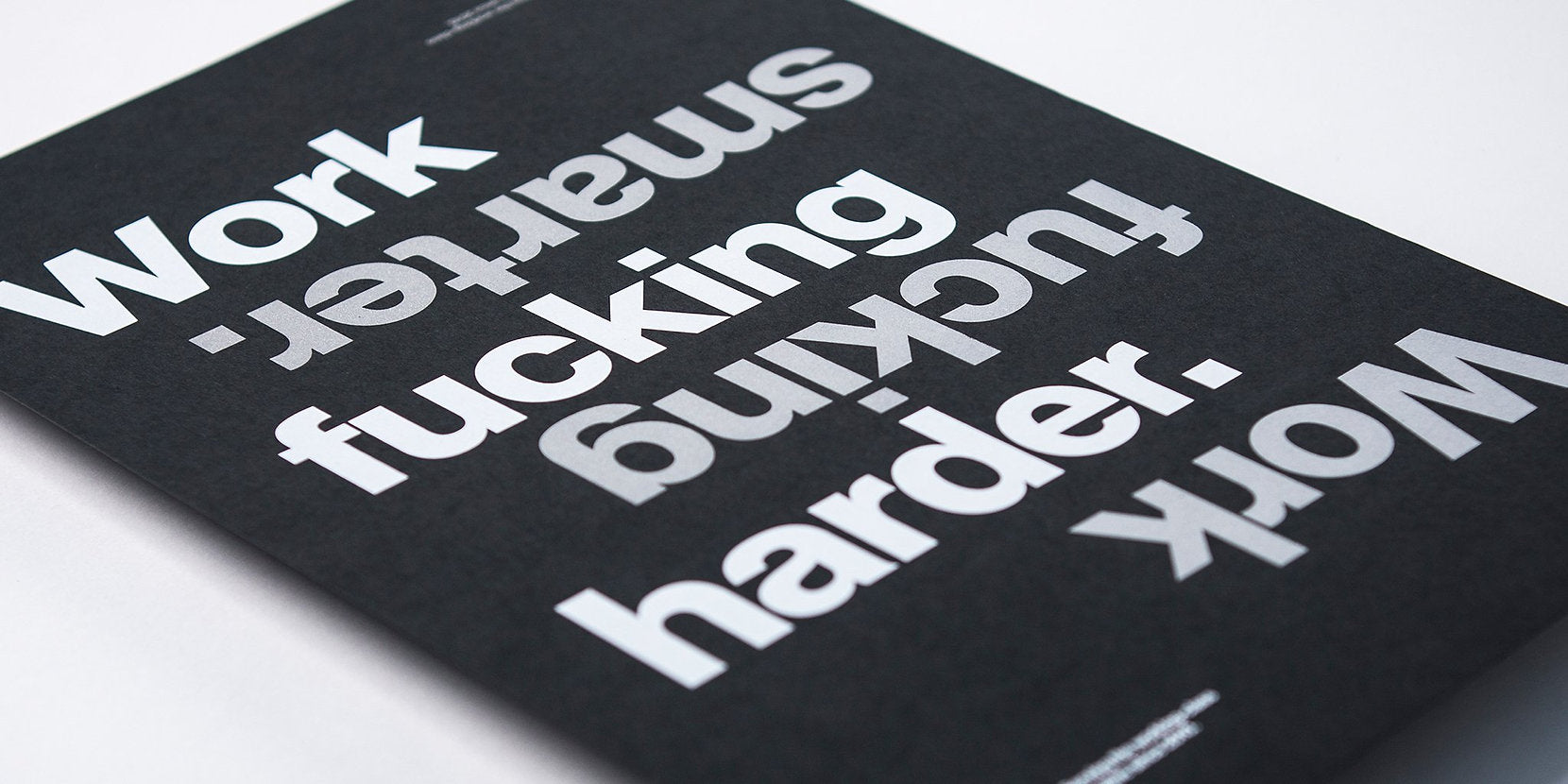 gfda poster on black paper with silver and white text, text states work fucking smarter, work fucking harder, close up of  the text