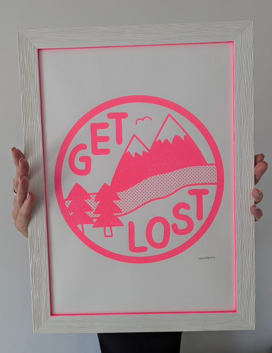 Framed print with 'Get Lost' design held by a person against a gray background