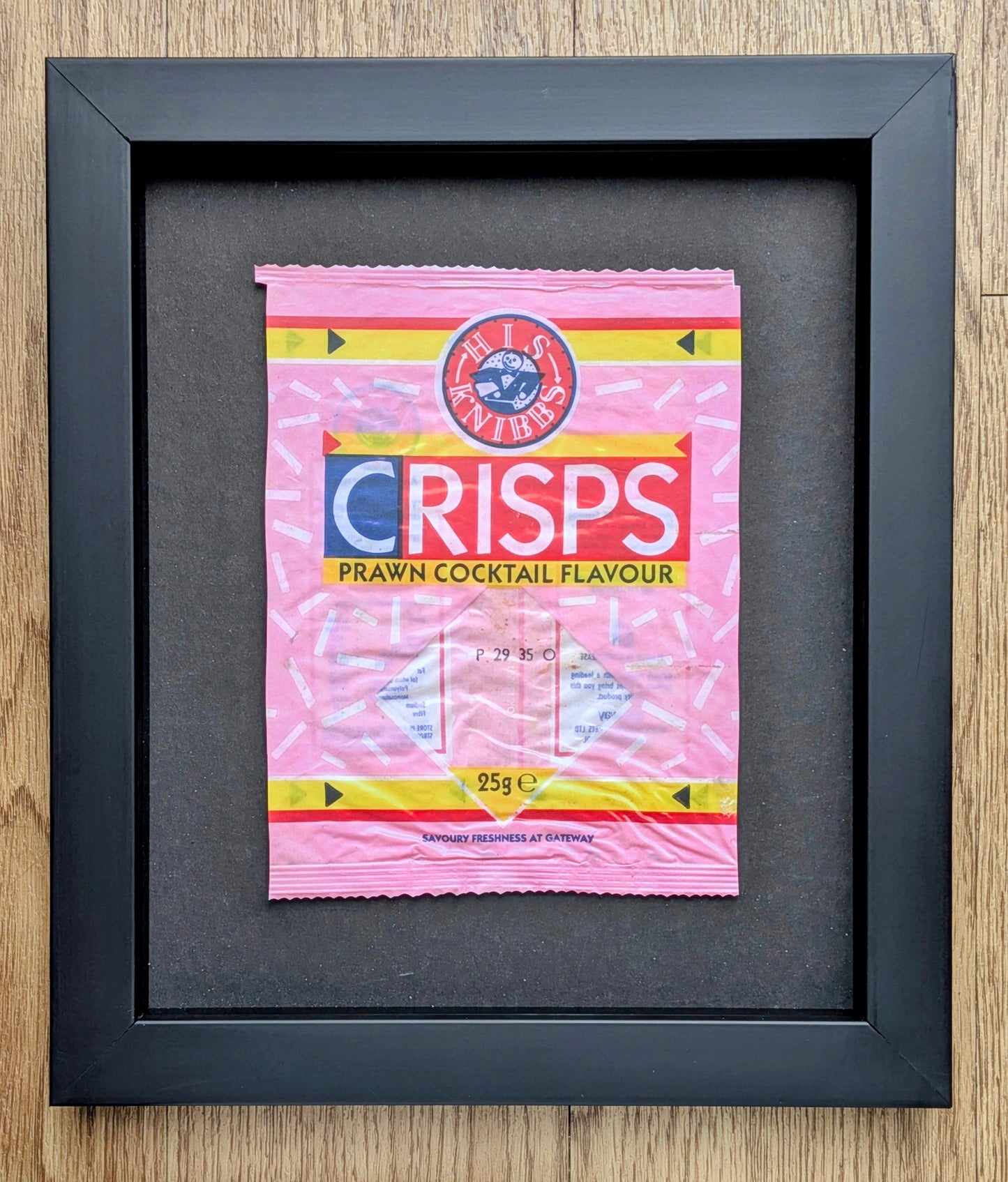 Framed picture of a pink crisps packet on a wooden surface