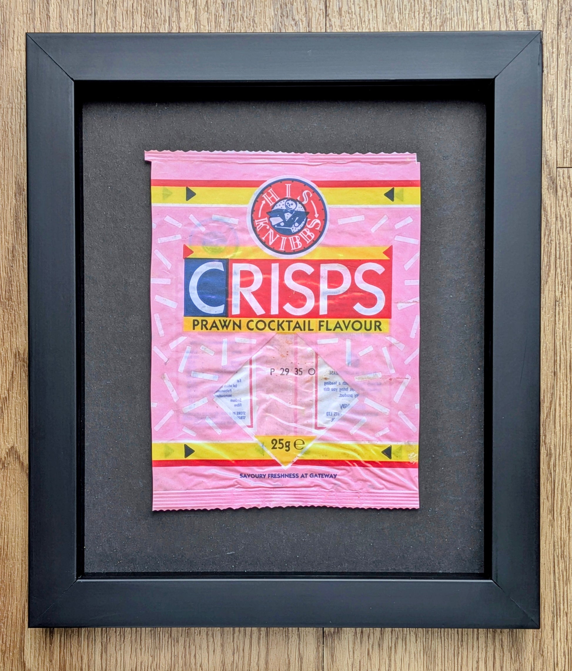 Framed picture of a pink crisps packet on a wooden surface