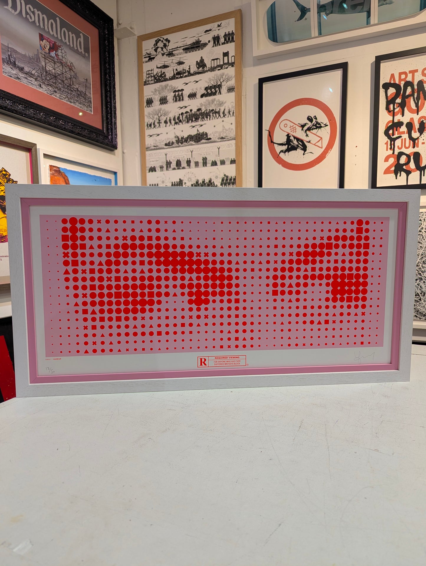 Framed artwork with red and white design on a white surface, surrounded by other framed pictures.