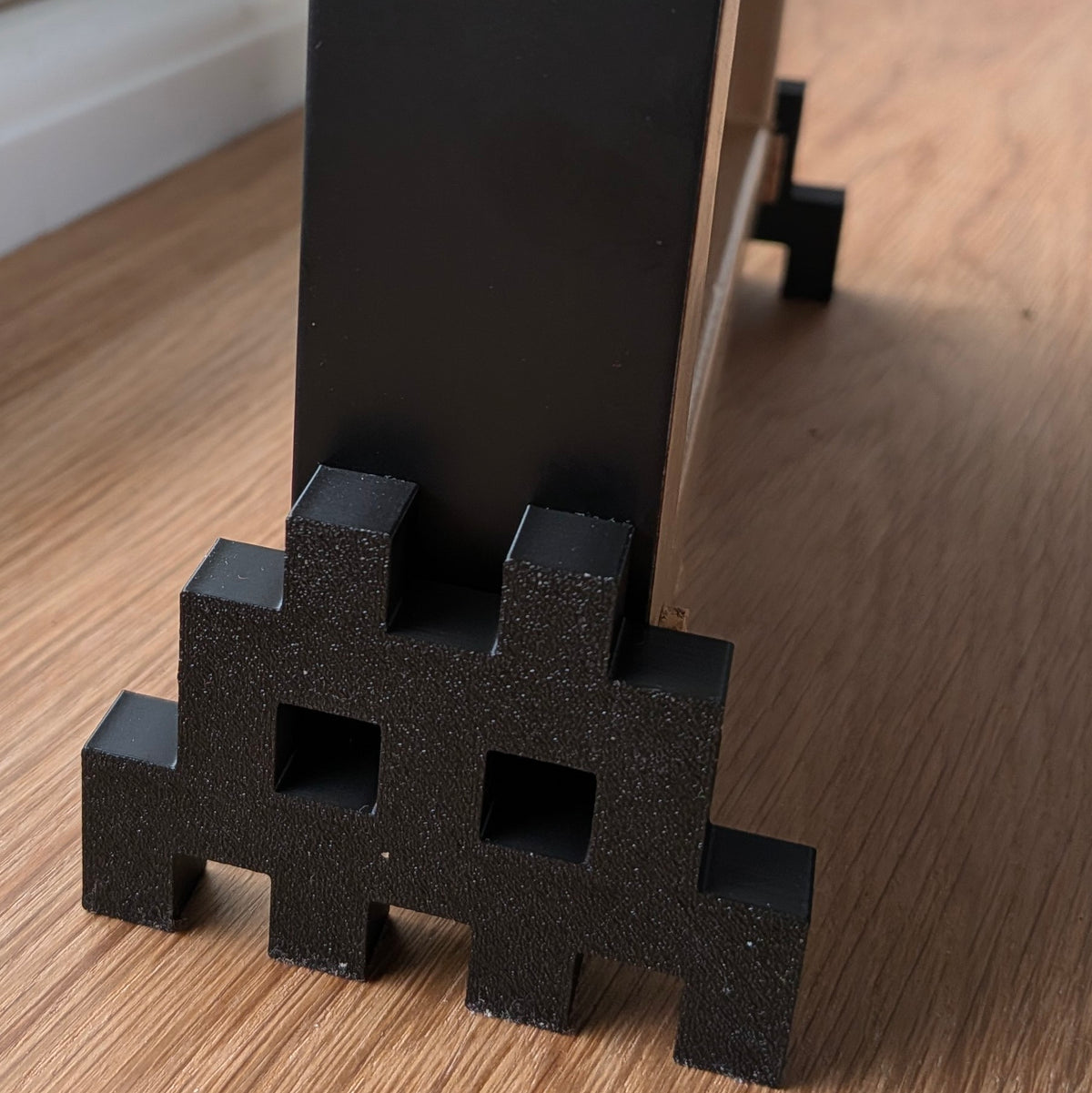 invader shaped character 3d printer foot for picture frame on a wood background