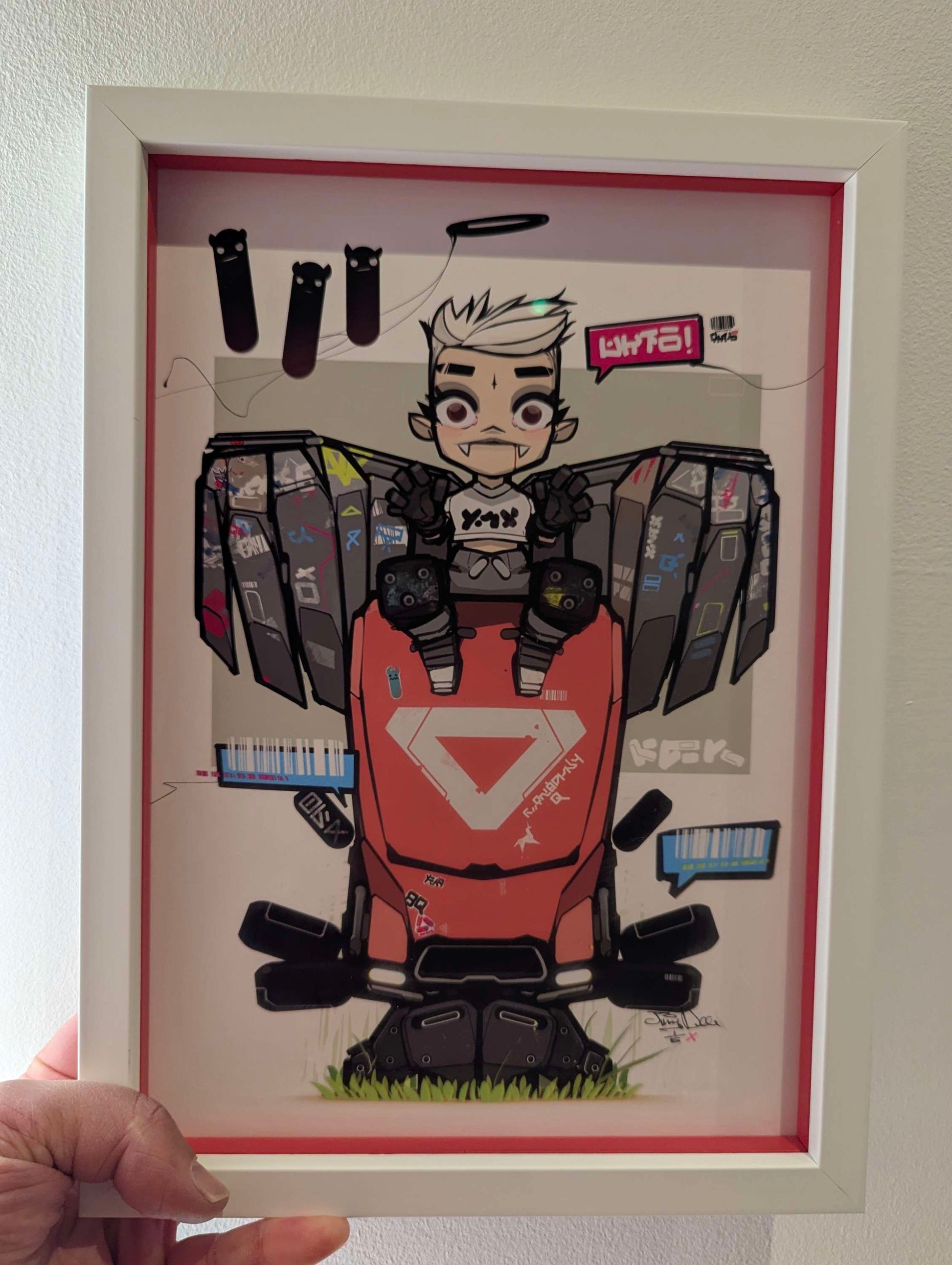 frame anime style character sat on  red robot, the character has grey wings and vampire teeth, the frame is white with a colour matching slip. picture frame is being held hand is showing