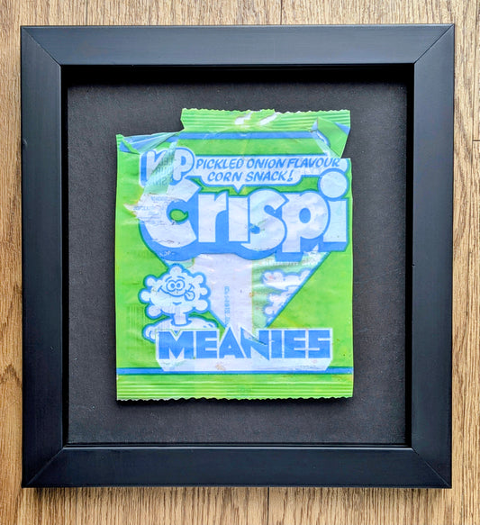 Framed green and blue packet of Crispi Meanies snacks on a wooden surface