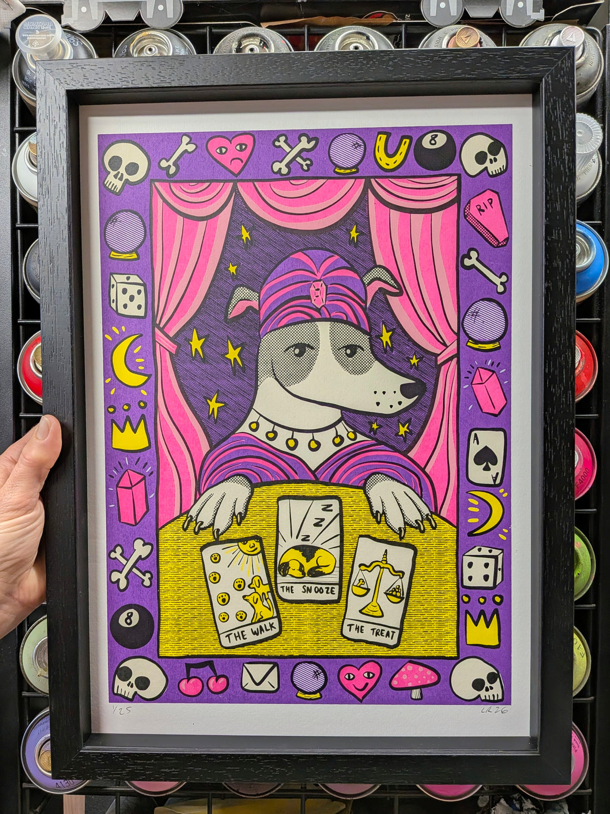 a dog dressed as a tarot card reader surrounded by skulls. cards and dice in a black wood grain frame. spray can background