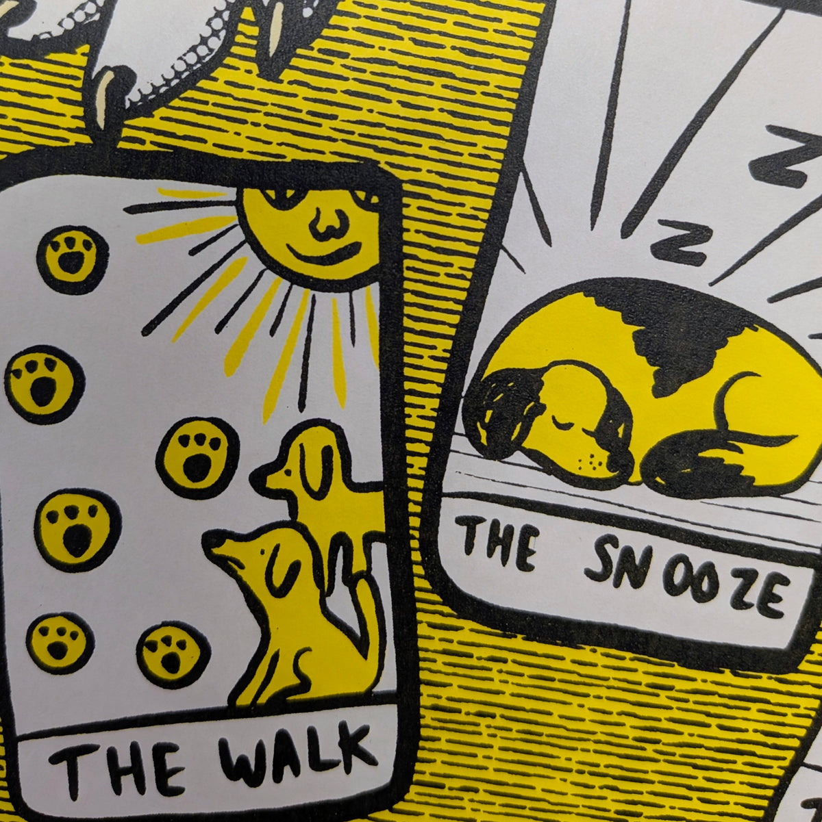 A close-up of a printed illustration featuring two cartoon dog cards labeled 'THE WALK' and 'THE SNOOZE' on a yellow patterned background.