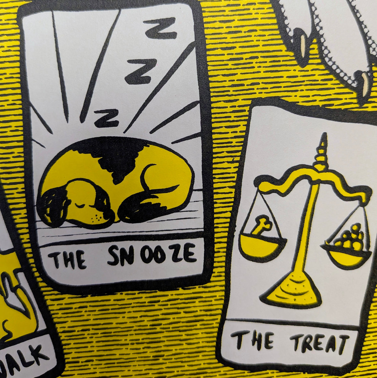 A close-up of a printed illustration featuring two cartoon dog cards labelled 'THE TREAT' and 'THE SNOOZE' on a yellow patterned background.