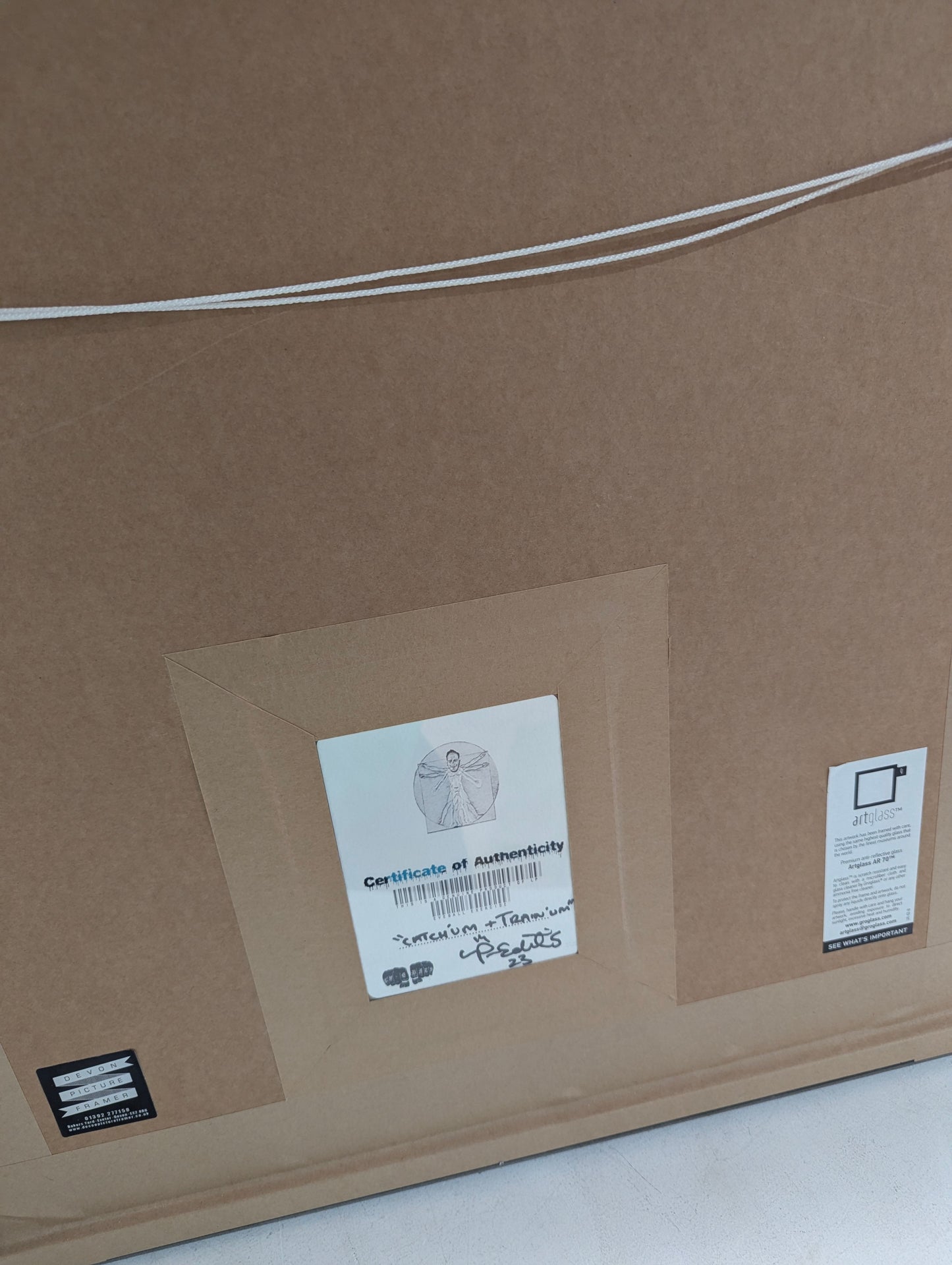 Back of a framed artwork with a certificate of authenticity and other labels.