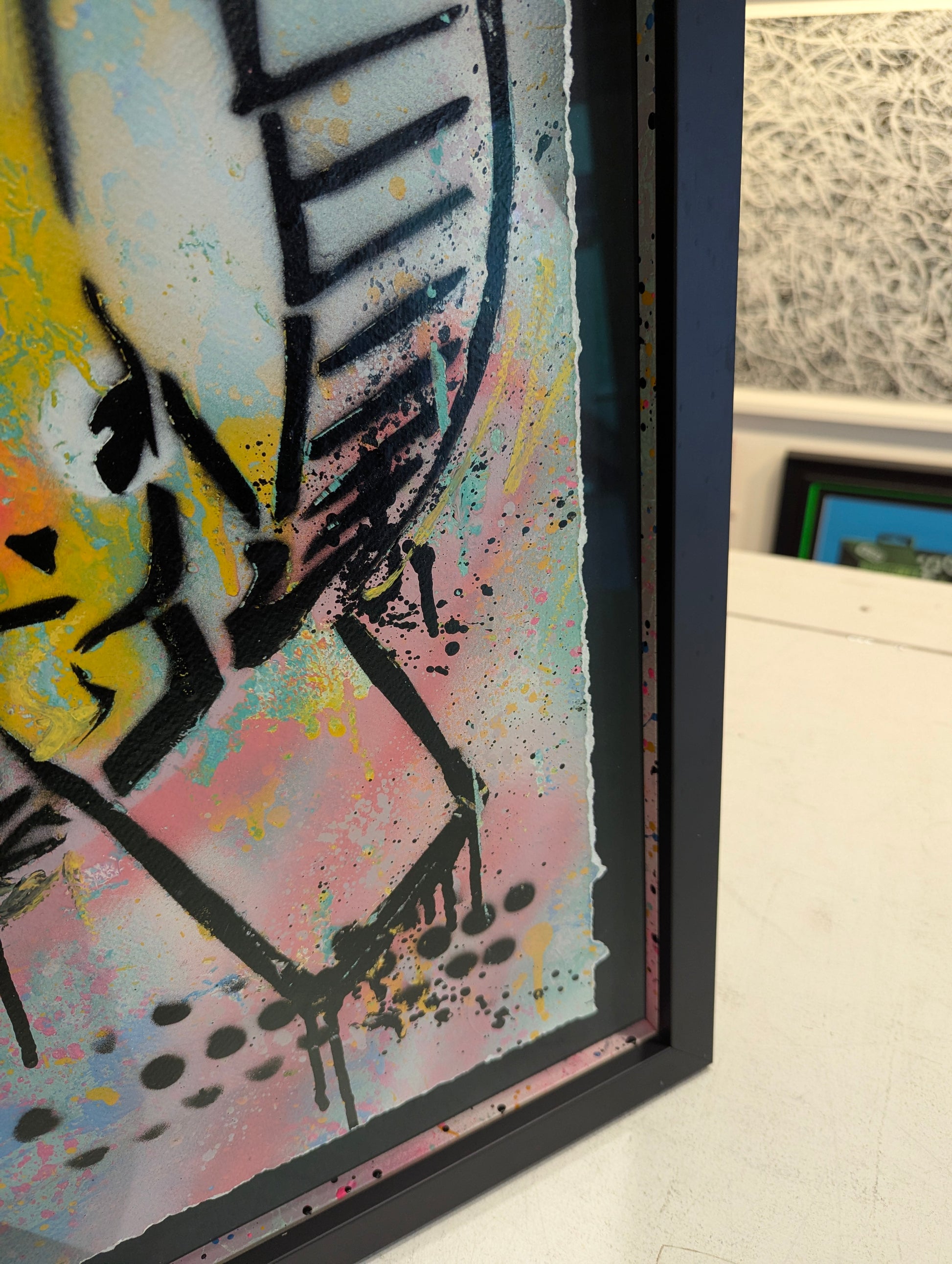 Framed abstract artwork with colorful splashes and black lines on a white surface.