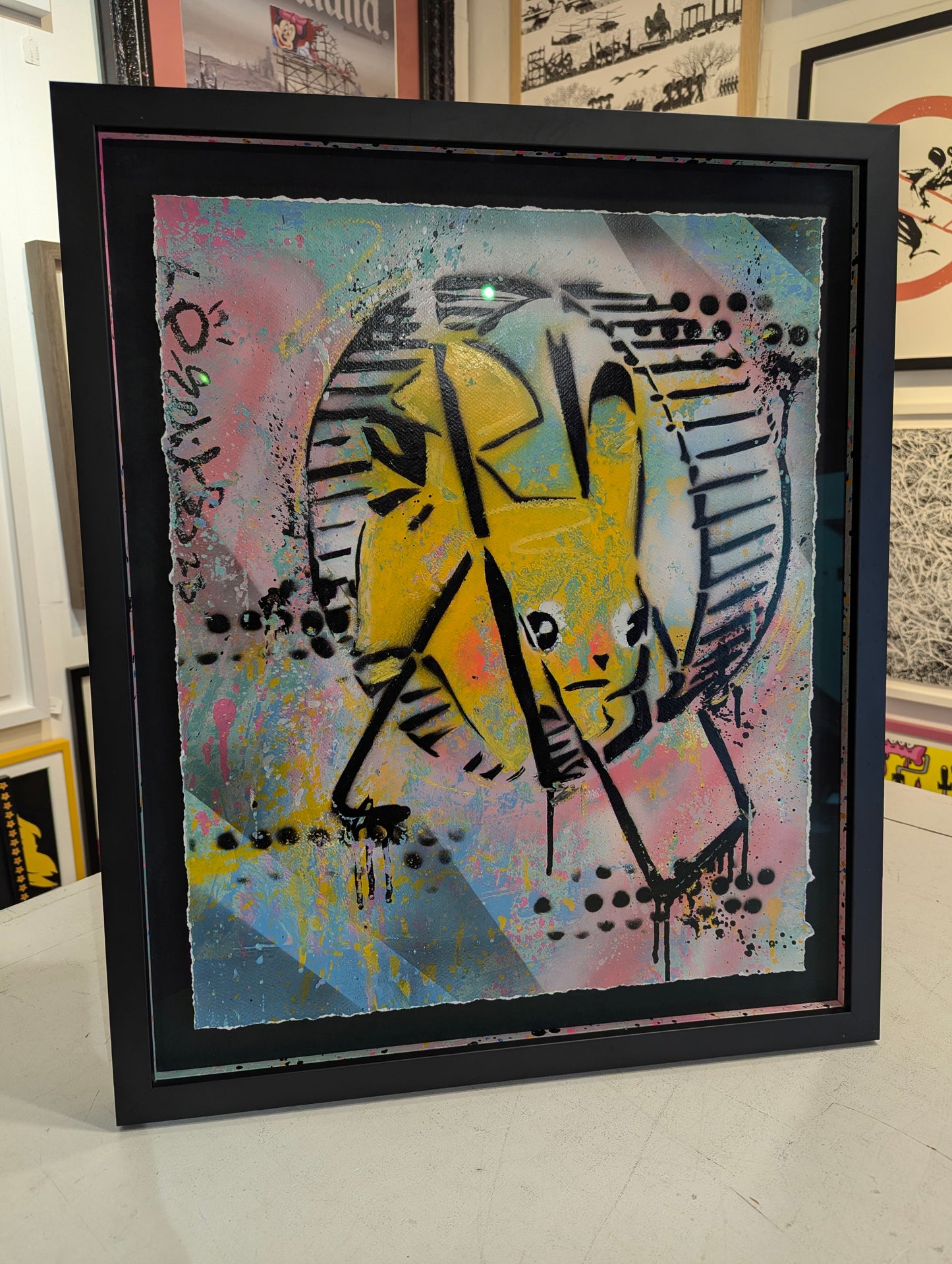 Framed abstract artwork with a yellow and black design on a colorful background.