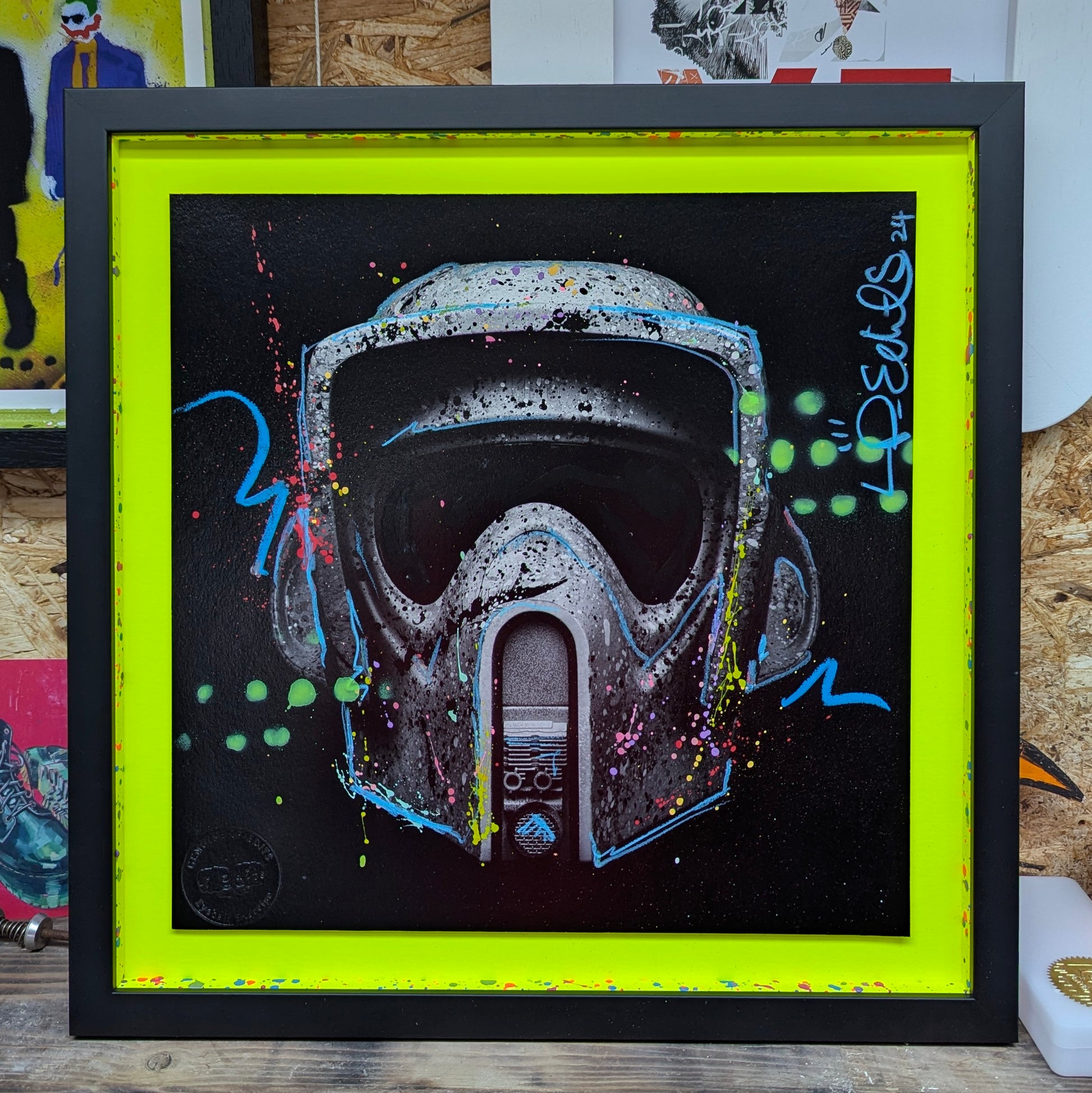 lp edits tree hugger float mounted on bright neon yellow card, frame is smooth black with yellow slips that have been splattered with pink blue purple paint, artwork is resting on wood shelf