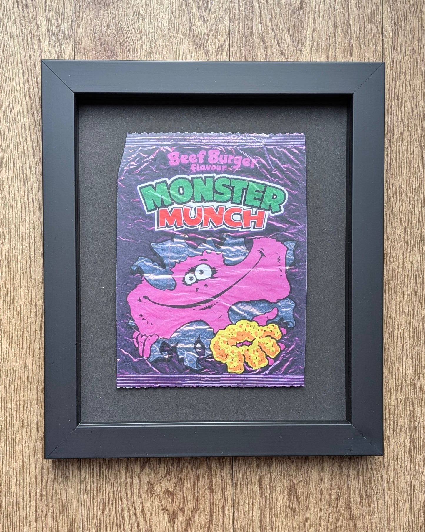 Framed Monster Munch snack packet on a wooden surface