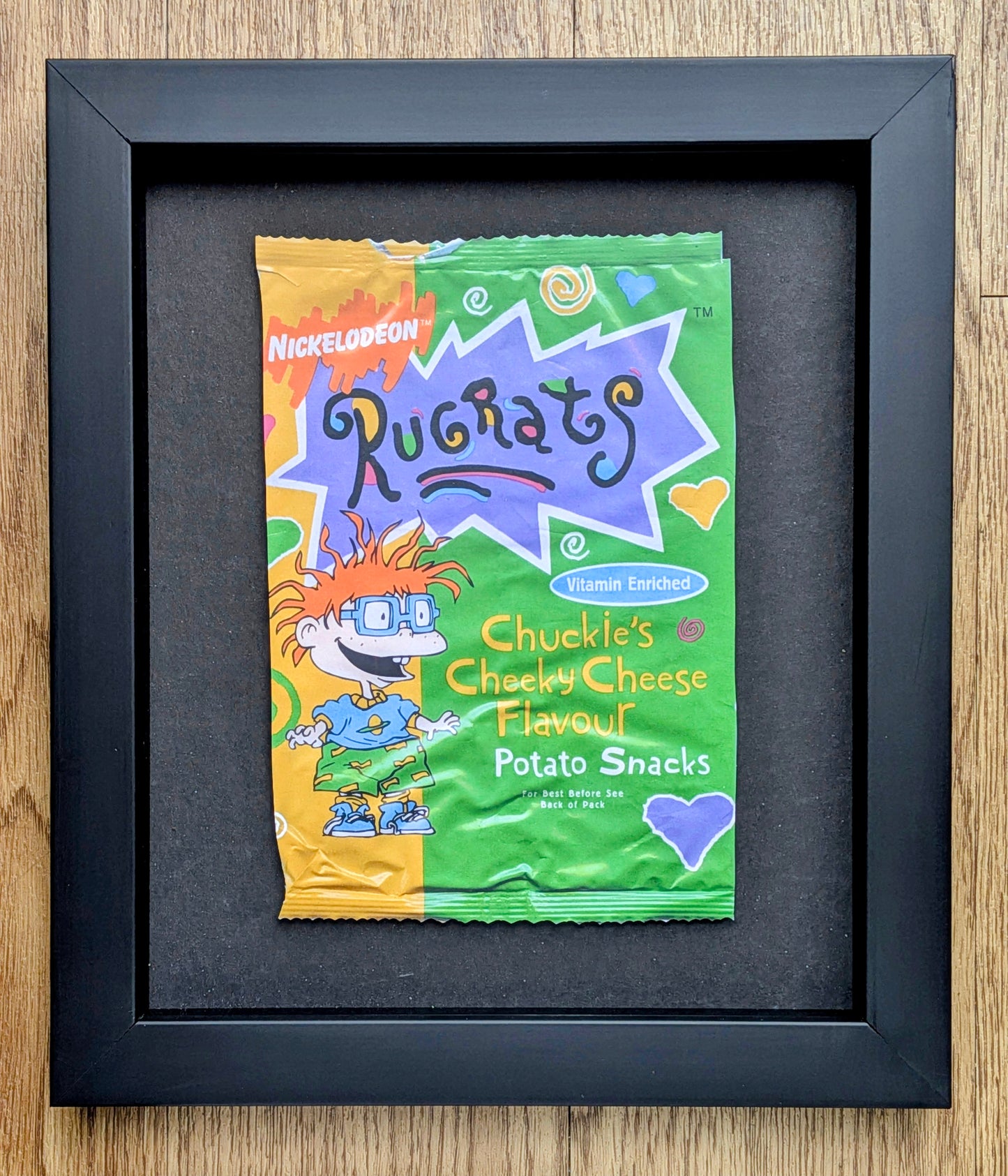 Framed Ruchats Chuckle's Cheeky Cheese Flavour potato snack packet on a wooden surface