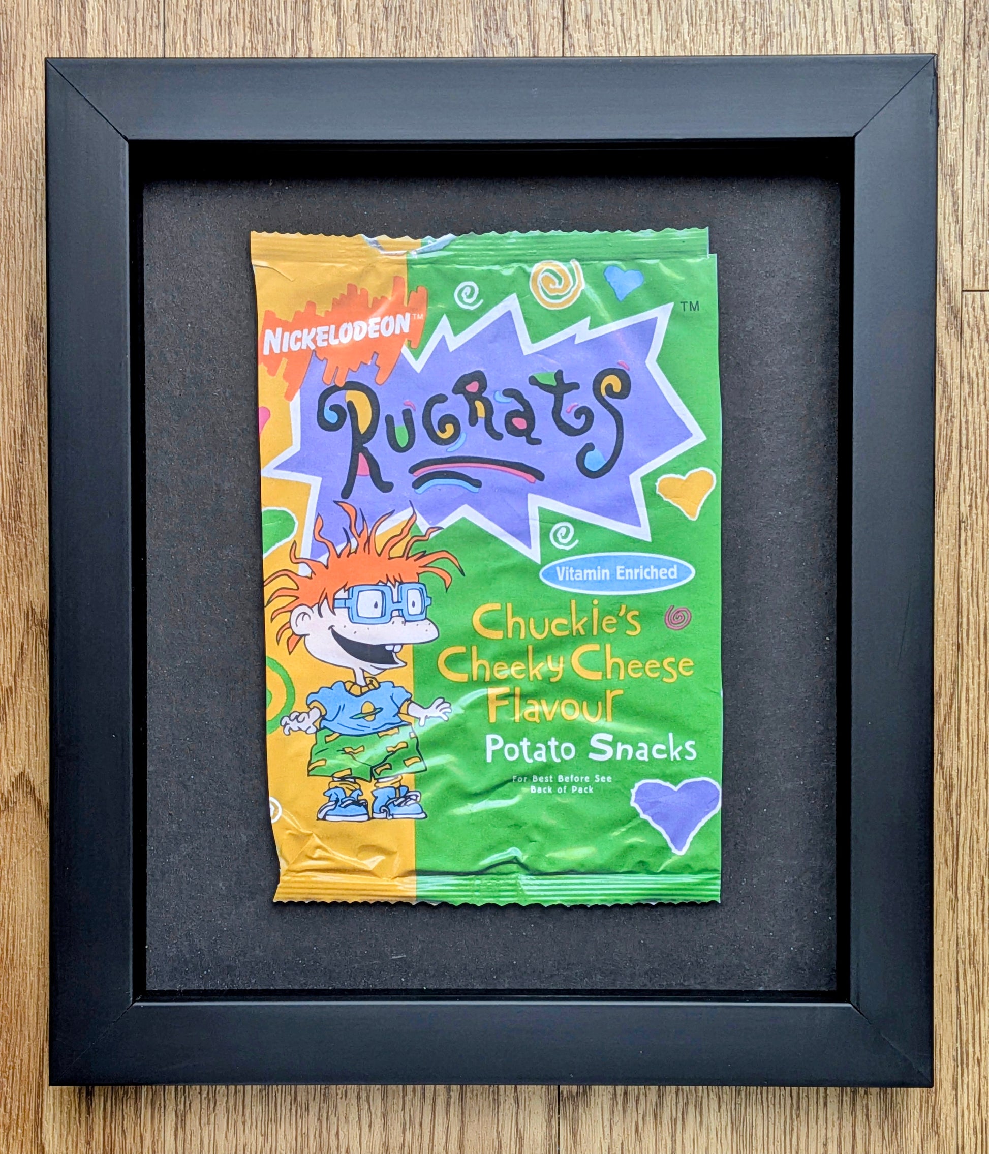 Framed Ruchats Chuckle's Cheeky Cheese Flavour potato snack packet on a wooden surface