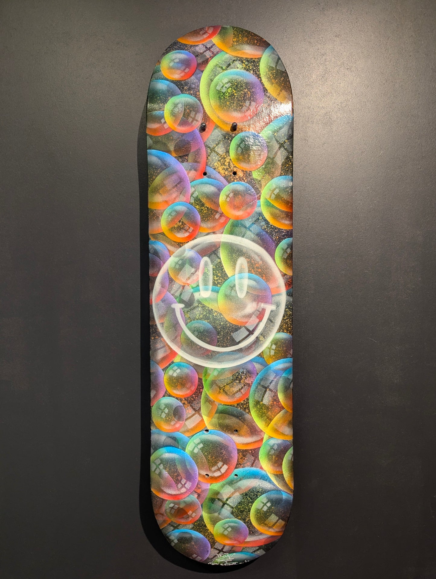 Skateboard deck with colorful bubble design and smiley face on a gray background