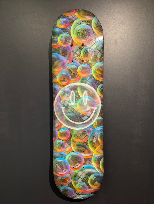 Skateboard deck with colorful bubble design and smiley face on a gray background