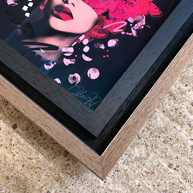 close up of picture frame, double frame, internal frame is black wood grain. outer frame is a brown tray frame style with a black shadow gap. print shows olly howe signature. picture is sat on concrete floor.