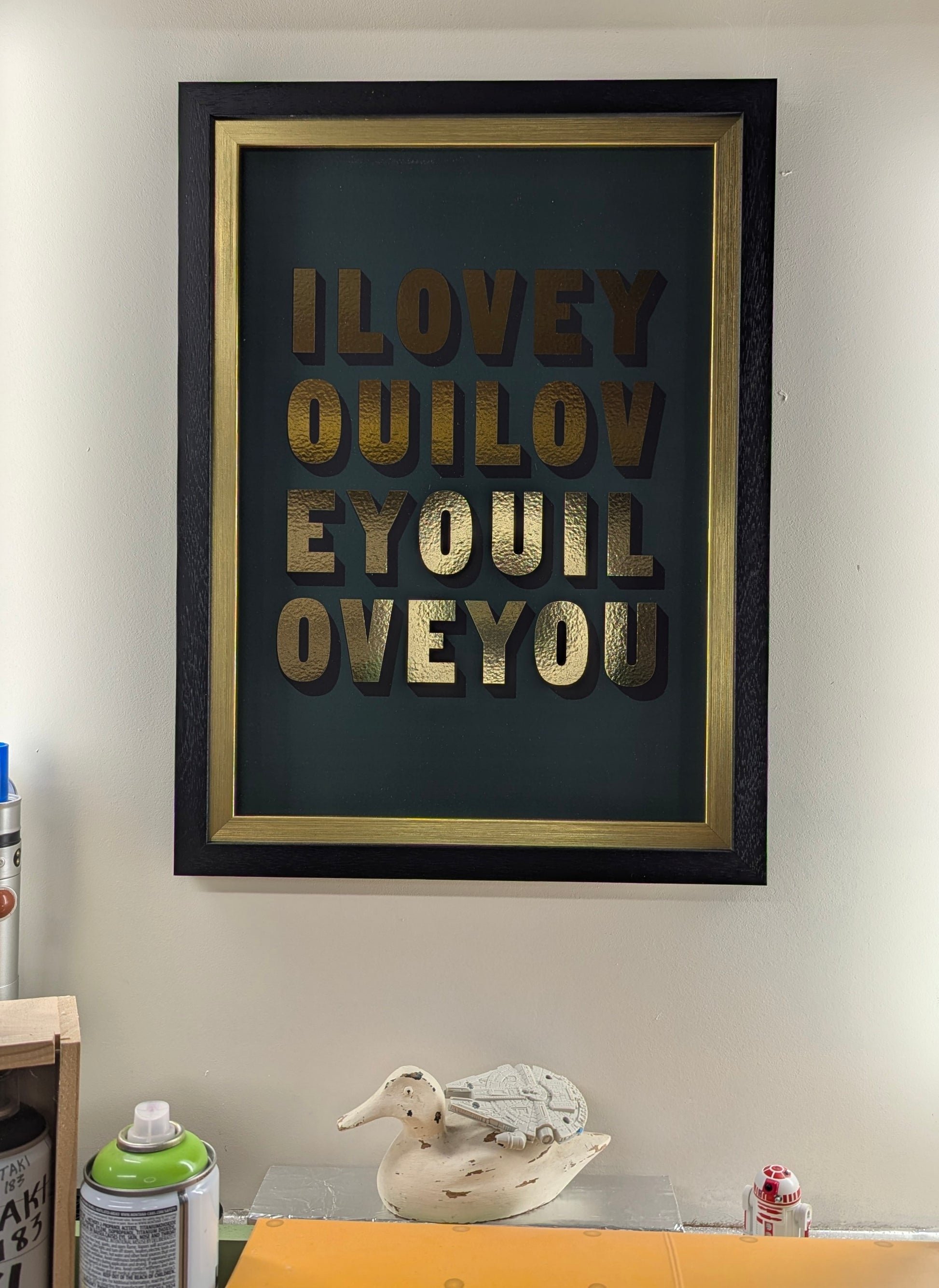 Framed artwork with 'I LOVE YOU' text on a wall with a duck and small millennium falcon on its back 