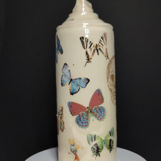 video of ceramic spray rotating on base, can is by Adam Graddon, spraycan is cream ceramic with colourful butterflies