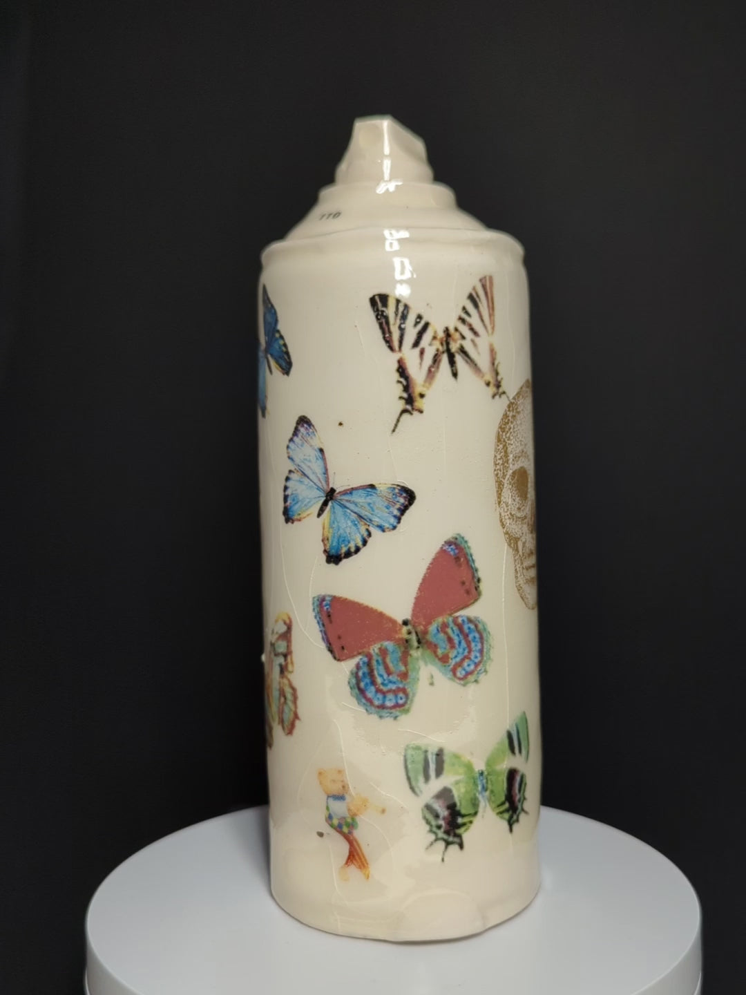 video of ceramic spray rotating on base, can is by Adam Graddon, spraycan is cream ceramic with colourful butterflies