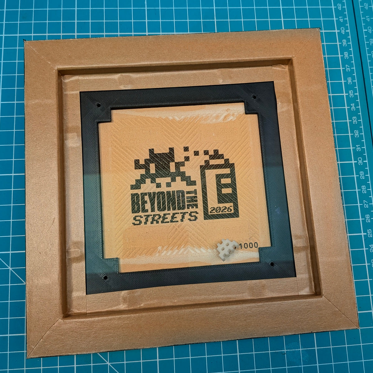 rear of picture frame, invader tile is by beyond the streets stamped on back against a cutting mat background