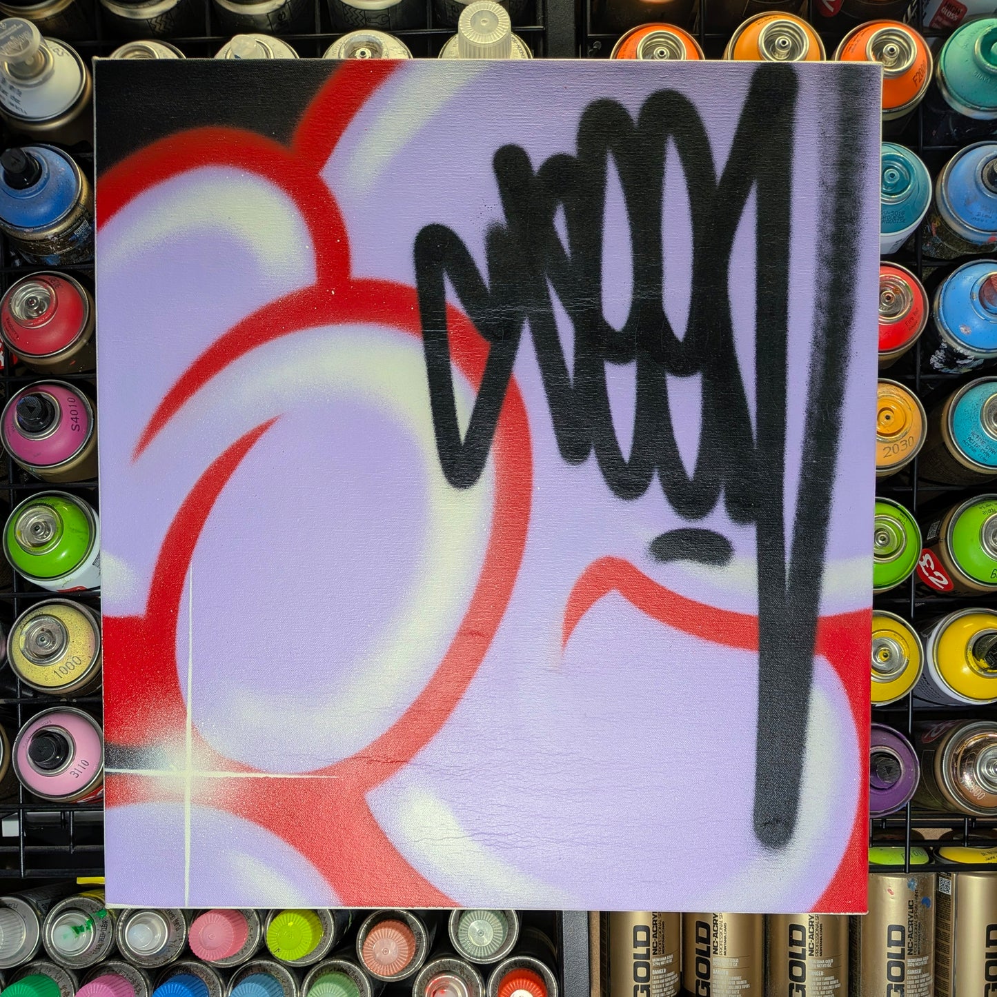 A square art print or canvas featuring abstract graffiti-style spray paint artwork, with bold black lettering and red, white, and black painted forms on a pale lavender background. The print is centered against a background filled with rows of colorful spray paint cans.