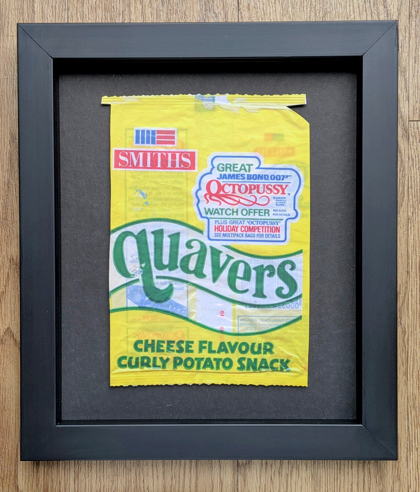 Framed yellow Quavers snack packet on a wooden surface