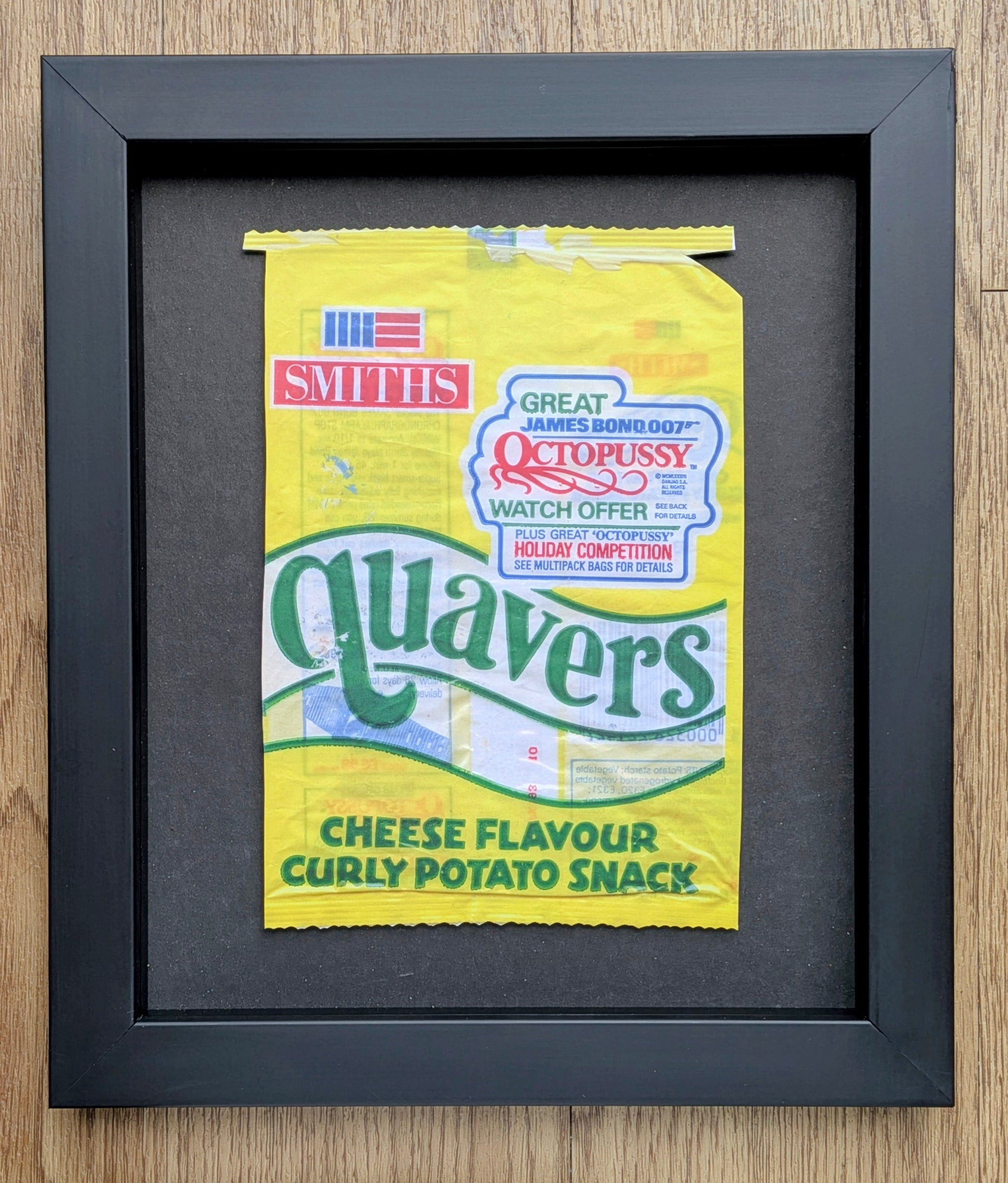 Framed yellow Quavers snack packet on a wooden surface