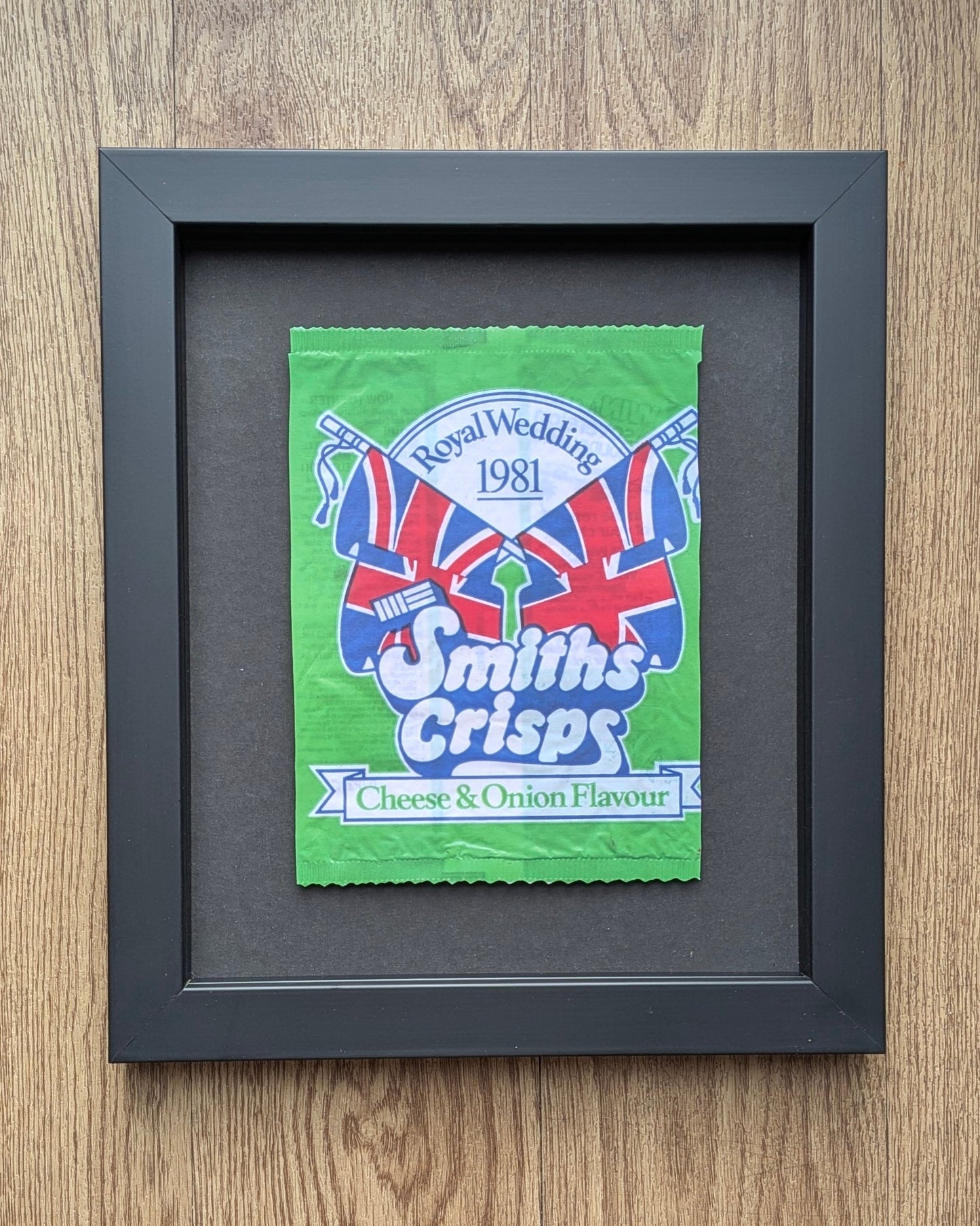 Framed Smiths Crisps packet with Union Jack design on a wooden surface
