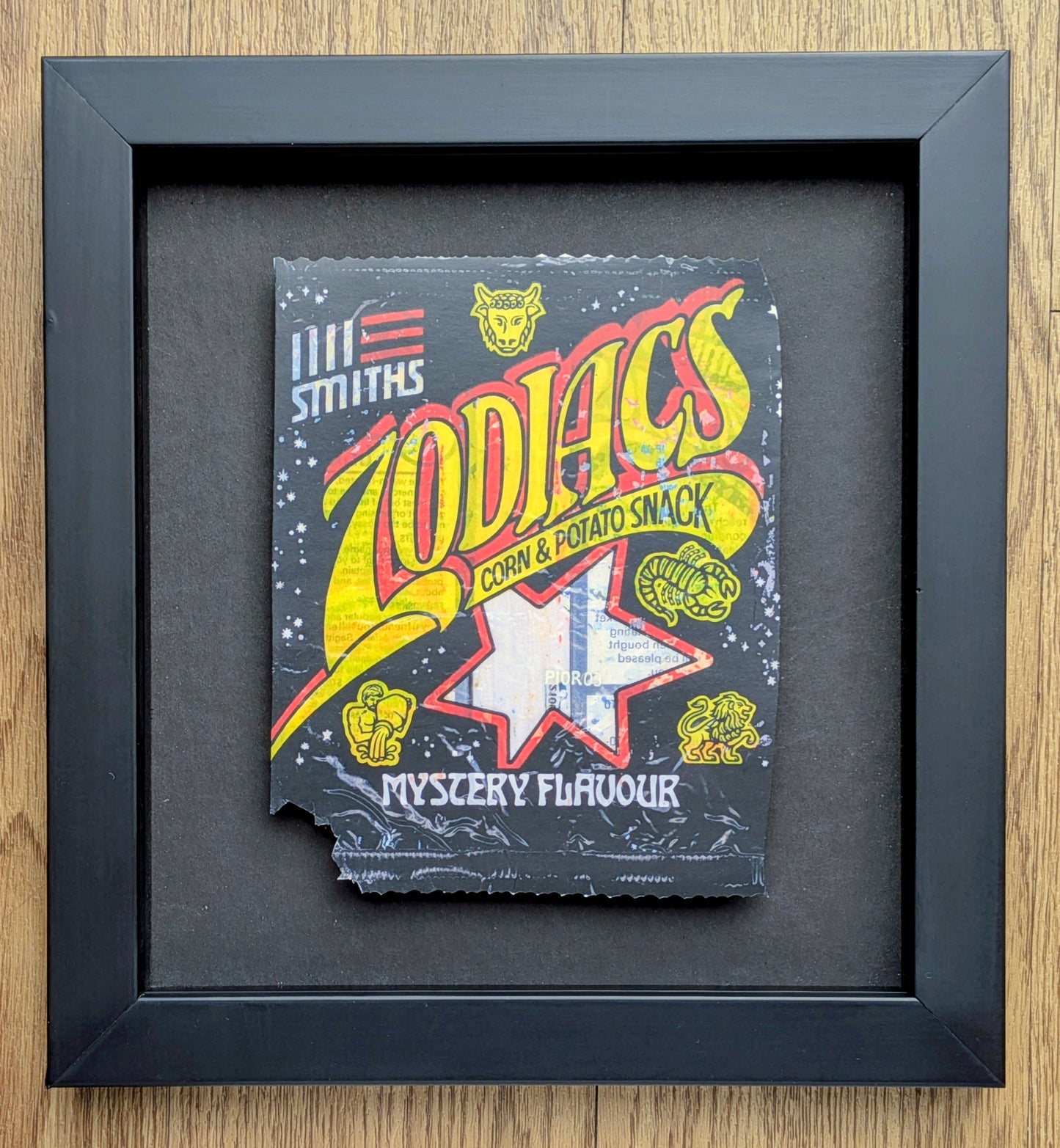 Framed vintage-style packaging of 'Zodiacs' corn and potato snack with colorful text and graphics.
