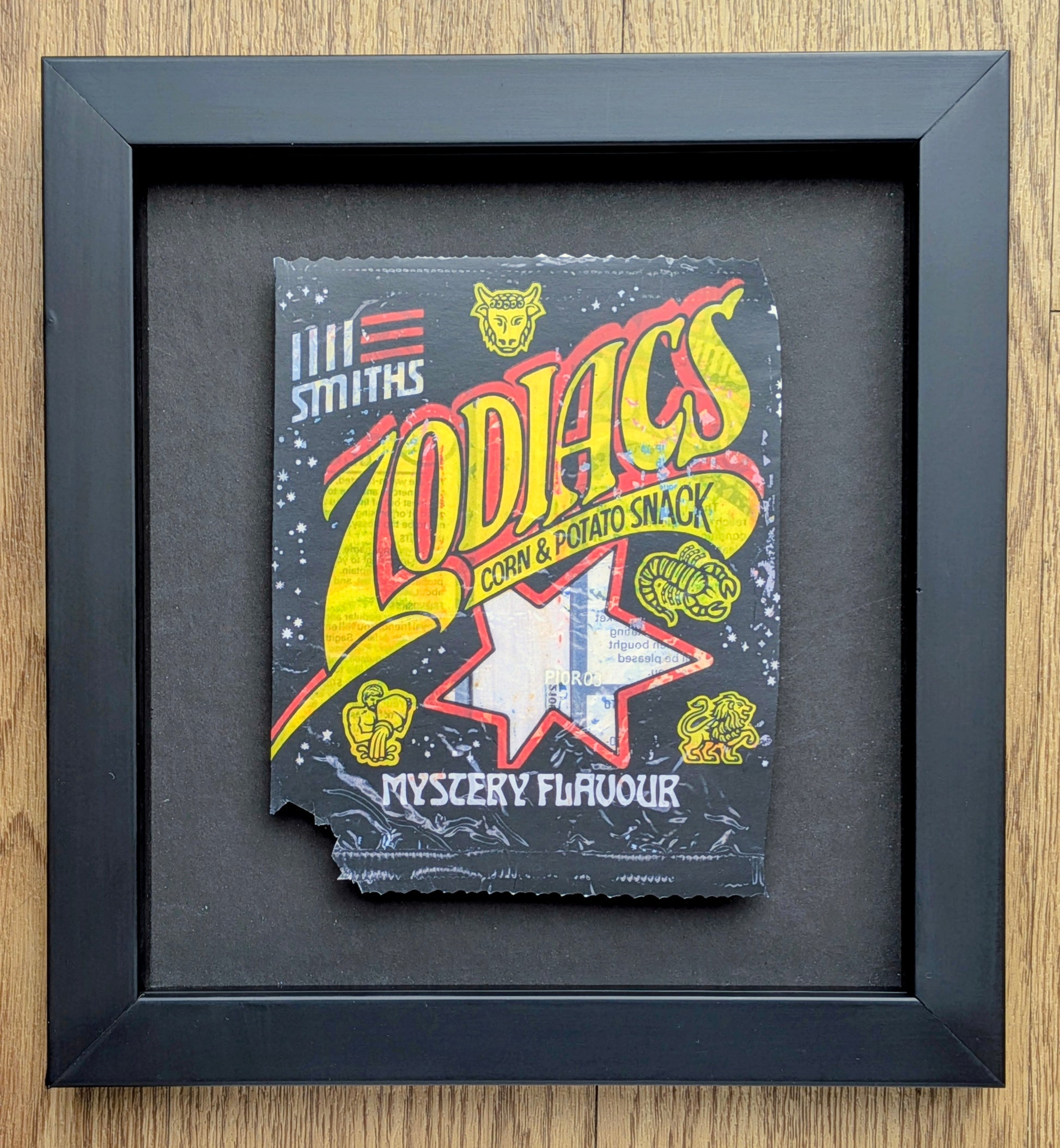 Framed vintage-style packaging of 'Zodiacs' corn and potato snack with colorful text and graphics.