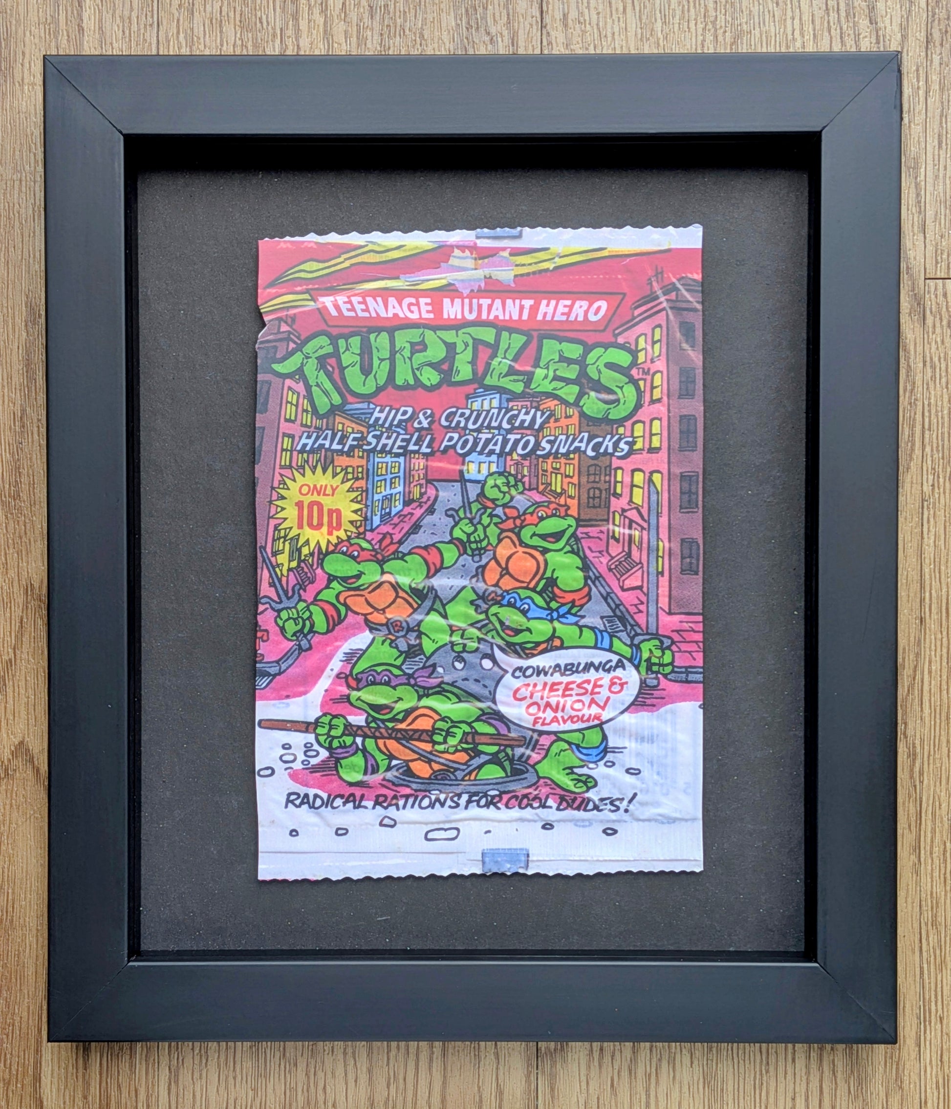 Framed poster of Teenage Mutant Hero Turtles potato snacks packaging on a wooden surface