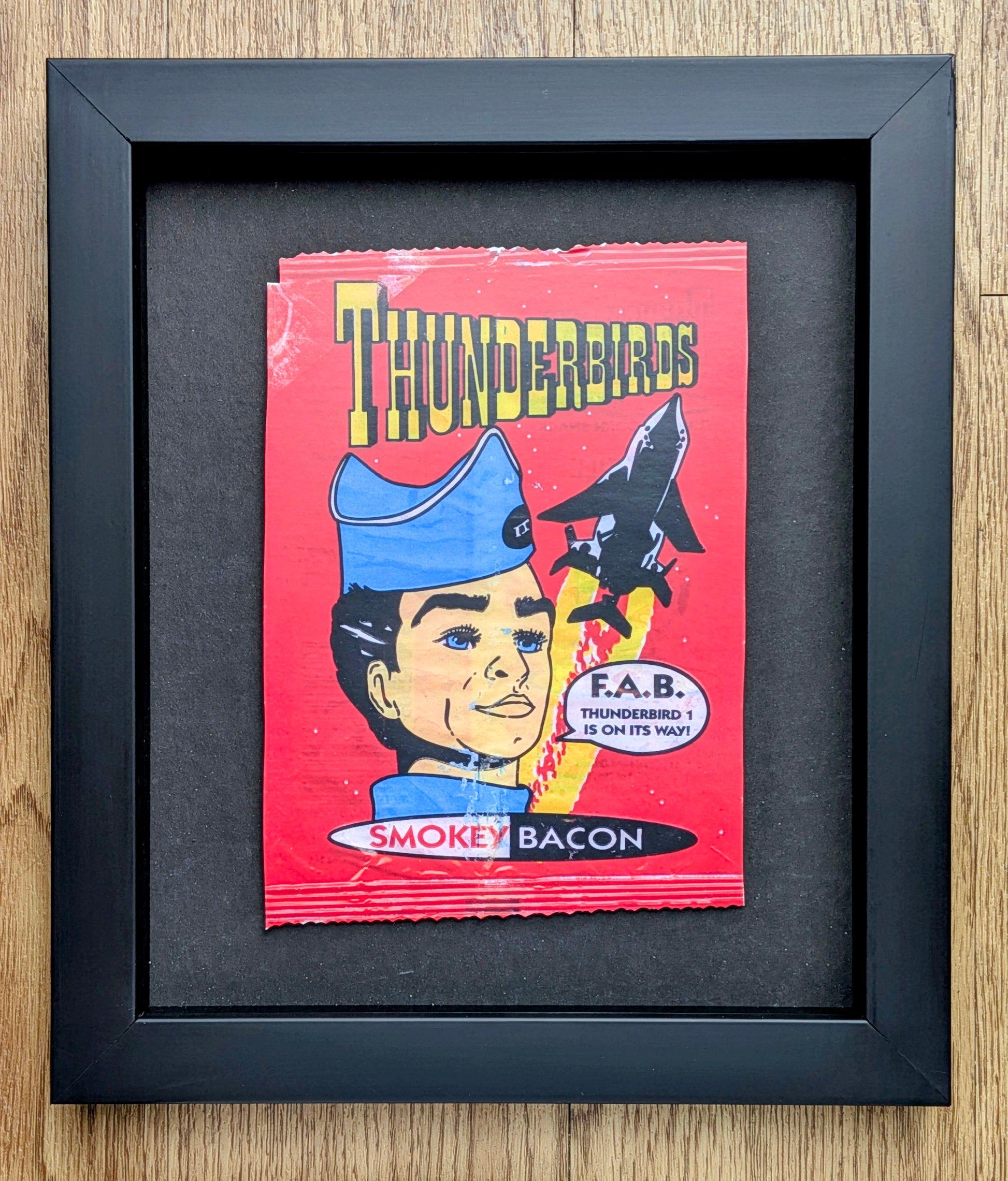 Framed Smokey Bacon Thunderbirds product packaging on a wooden surface