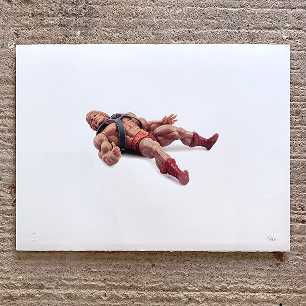 large print of he man plastic toy, front of toy on show, image is the only colour on white paper. paper is on concrete floor