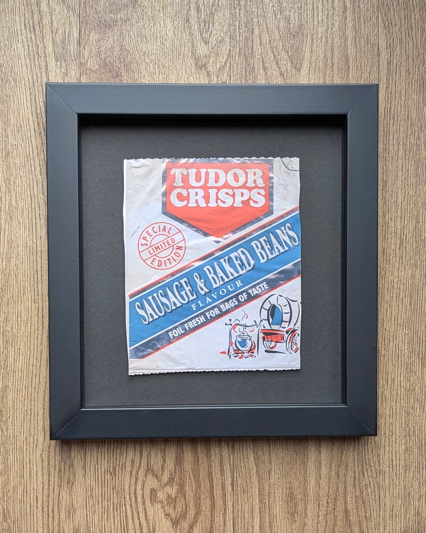 Framed vintage Tudor Crisps packet on a wooden surface