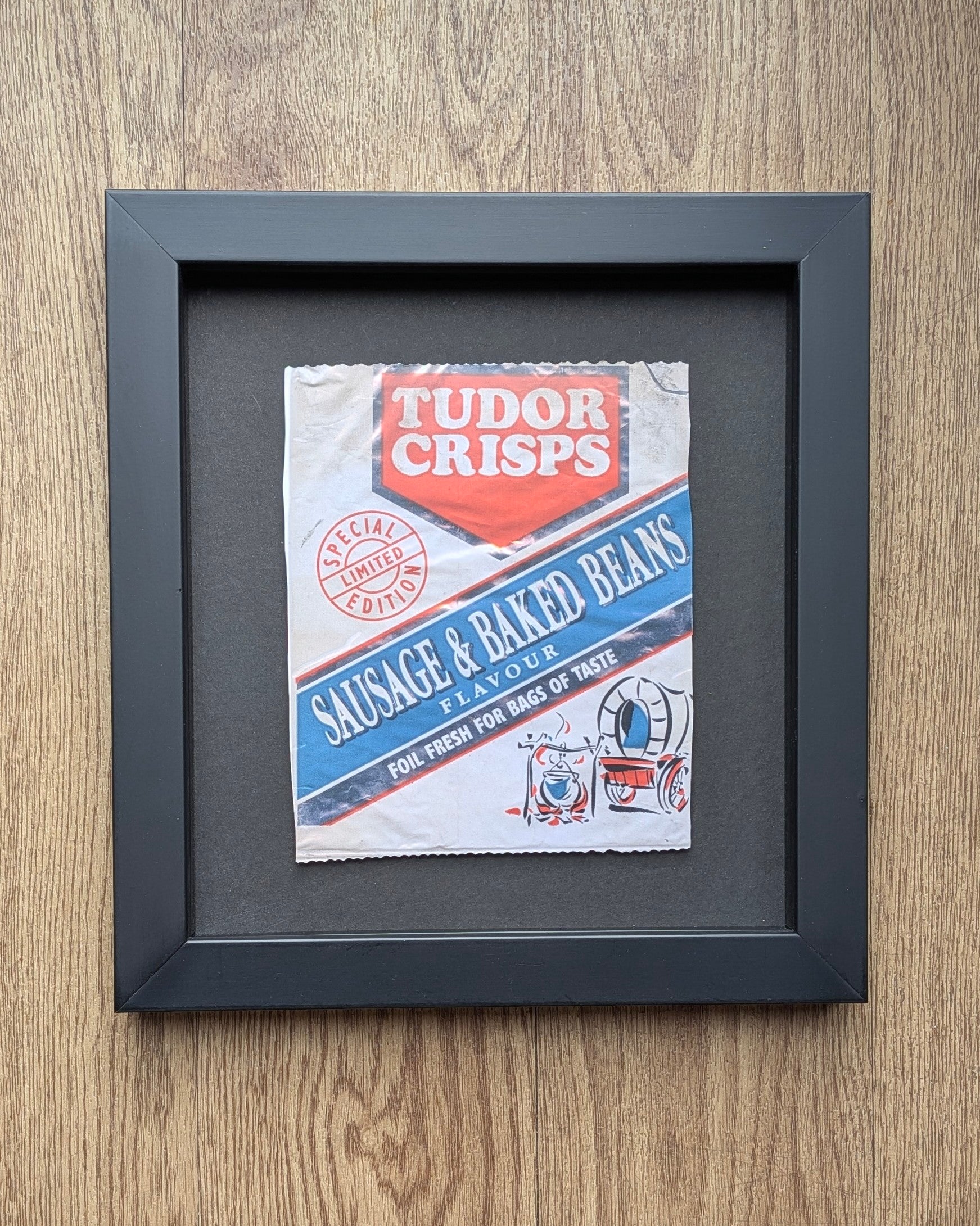 Framed vintage Tudor Crisps packet on a wooden surface
