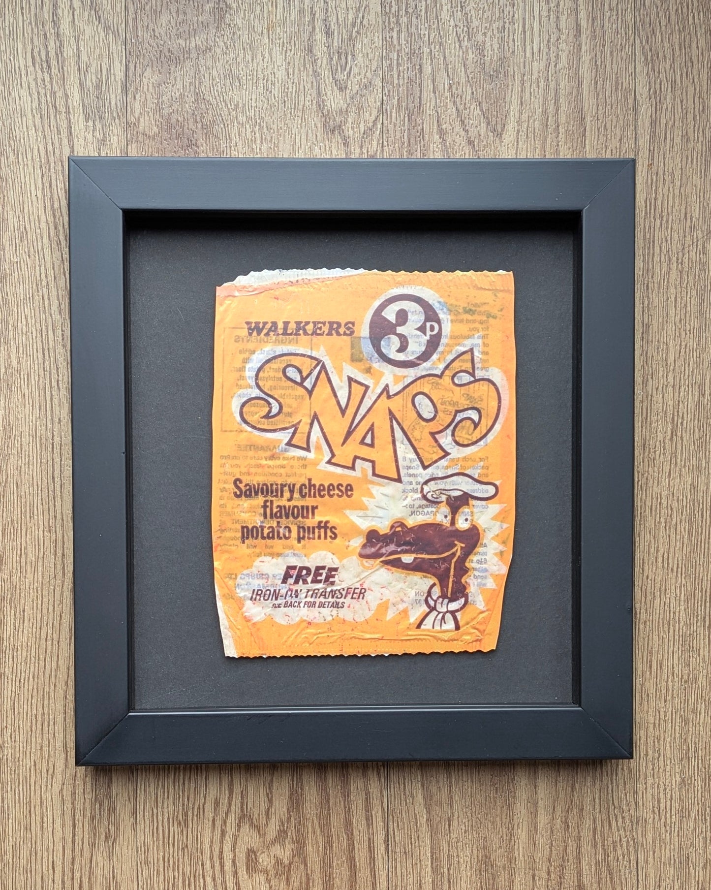 Framed picture of a vintage Walkers Snaps packet on a wooden surface