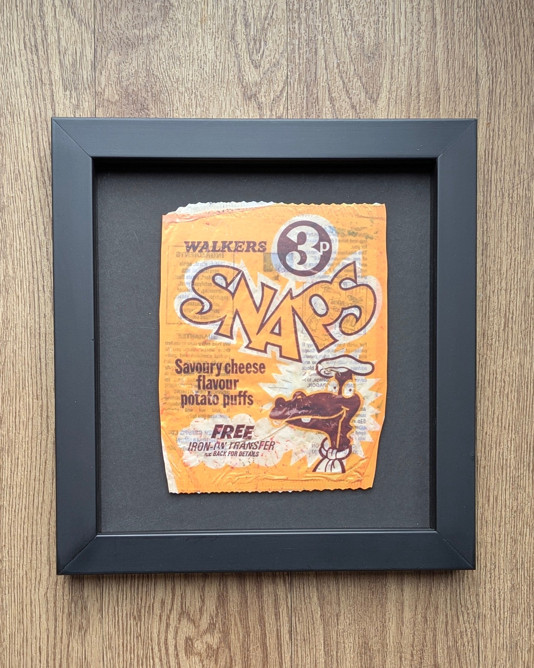 Framed picture of a vintage Walkers Snaps packet on a wooden surface